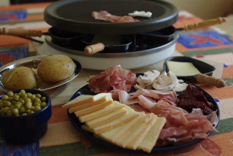 Raclette al centro della tavola con patate, prosciutto e funghi